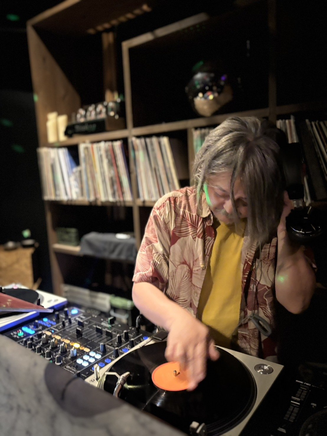 レコード棚の前でDJプレイするTSUYOSHI SASAKI
